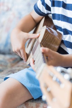 Beyaz çocuk küçük gitar ya da ukulele ile müzik akorları çalıyor ve yapıyor.