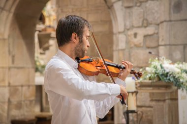Beyaz kemancı, klasik kıyafetler giyip kapalı bir yerde, kilisede gösteri yapıyor. Canlı performans. Kapat.