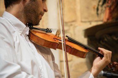 Beyaz kemancı, klasik kıyafetler giyip kapalı bir yerde, kilisede gösteri yapıyor. Canlı performans. Kapat.