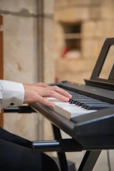 İç kilise ortamında klavyede müzik çalan klasik giysili beyaz bir adamın elleri. Kapat.