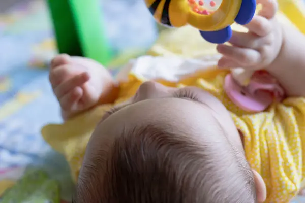 Sırtüstü uzanmış bebek oyuncağıyla etkileşime giriyor. Fiziksel ve duyusal gelişim, kavram.
