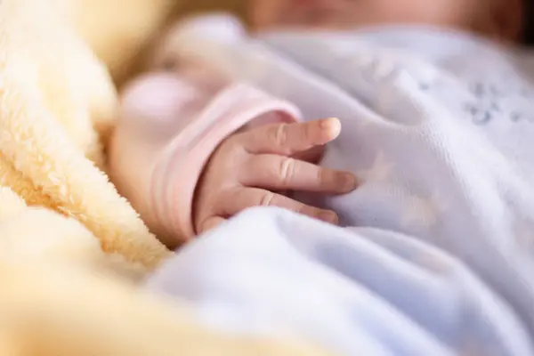 Kafkasyalı yeni doğmuş bebeğin renkli battaniyelerle rahat bir karyolada uyumasını kapatın. Onun narin, ince eline odaklan..