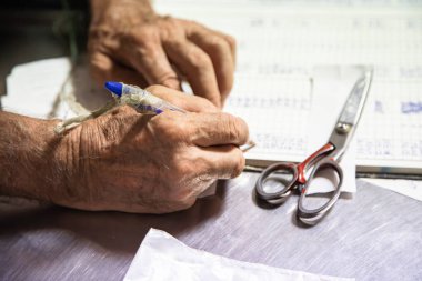 Kitapta kalemi tutan bir elin yakın çekimi. Muhasebe işlerini elle yapan yaşlı bir adamın eli. Aktif yaşlanma konsepti, el yazısı. Yatay resim.