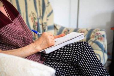 Not defterine yazı yazan birinin fotoğrafını çek. Yetişkin bir insan kanepede oturup mürekkep kalemi ve not defteriyle bir mesaj yazar. Yazarlık alıştırmaları, yaratıcı yazma kavramı.