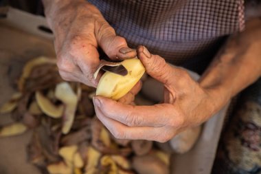 Yaşlı bir kadının elleri patates soyarak ev işi yapıyor. Eklem iltihabı ve kemik iltihabı olan yaşlı eller. İlgili hastalıklara rağmen aktif yaşlanma kavramı. Kapat.