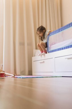 Küçük beyaz kız yatak odasında oynuyor, yataktan kalkıp kalkınca motor becerilerini geliştiriyor. Boşluğu kopyala