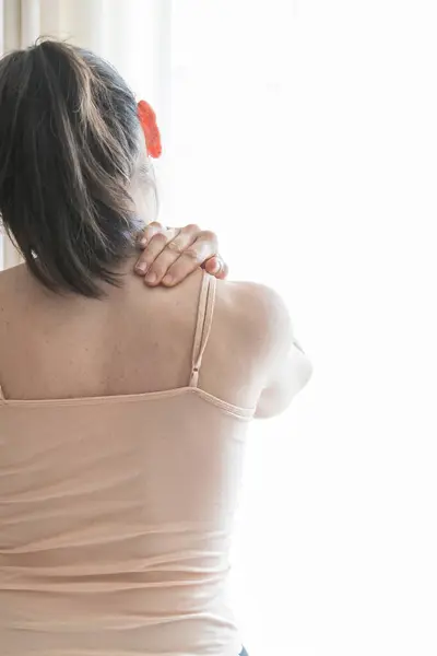 Genç, beyaz bir kadın sırtüstü oturmuş boynunda, omuzlarında ve sırtında ağrı olduğunu söylüyor. Kapat ve boşluğu kopyala.