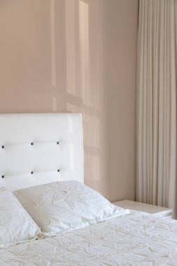 Yastık ve yatak başlıklı parlak bir yatak odasının iç kısmı. Çok rahat, rahat ve modern. Duvardan içeri ışık giriyor. Beyaz ve pastel tonlarda. Boşluğu kopyala