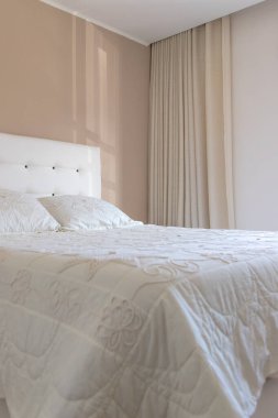 Yastıklı, yatak başlıklı, perdeli ve battaniyeli, çok rahat, rahat ve modern, duvardan içeri ışık giren parlak bir odanın ayrıntıları. Beyaz ve pastel tonlarda. Boşluğu kopyala
