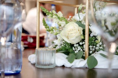 Beyaz gülleri, papatyaları, çingeneleri ve yeşillikleri olan güzel bir çiçek süsü. Ahşap bir çerçevede zarif bir şekilde düzenlenmiş. Sofistike ve büyüleyici bir yemek masası için mükemmel..