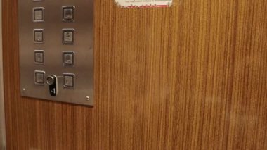 Eski bir asansörün içinde birinci katın düğmesine basan bir el hareketi..