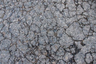 Close-up of a cracked asphalt surface, showcasing detailed texture and wear. The image captures the rugged and aged appearance of the pavement, highlighting natural deterioration over time. clipart