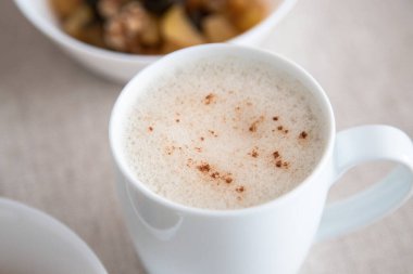 Lezzetli ve sağlıklı bir kahvaltıya eşlik etmesi için üzerine tarçın tozu dökülmüş beyaz bardak köpüklü kapuçino ya da sebze içeceği..
