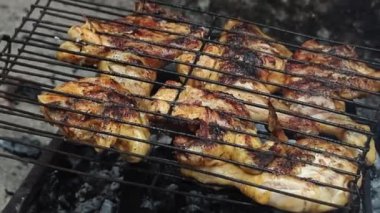 Yaşlı bir adam sulu ızgara yapar, baharatlı tavuk parçaları kızgın kömürlerin üzerinde ızgarada mükemmelce kızarır, kırsal bir açık hava barbekü deneyiminin özünü yakalar..