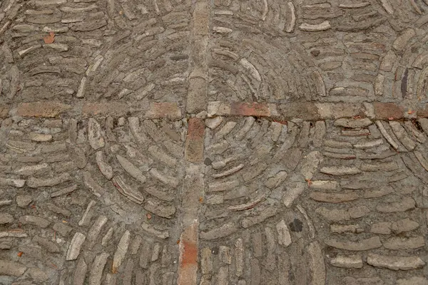 Çimentoya gömülü dairesel tuğla desenli taş kaldırıma yakın çekim. Karmaşık tasarım bu döşemenin dokusunu ve işçiliğini vurguluyor. Arkaplan resmi