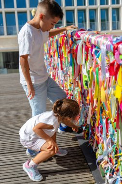 Arkadaşlık kurdeleleri. Ria de Aveiro köprüsünün kenarlarına iliştirilmiş güzel renkli kurdeleler, dostluğun ve aşkın sembolü. Aveiro, Portekiz. Çocuklar asılı kurdeleleri izliyor..