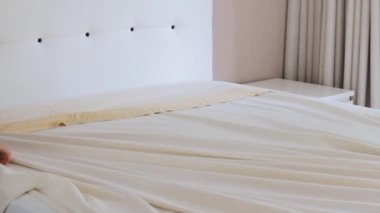 Bir insan çarşafları düzelterek, parlak, minimalist bir yatak odasında temiz ve düzenli bir uyku alanı yaratarak yatağı yapma görevini dikkatle yerine getirir..