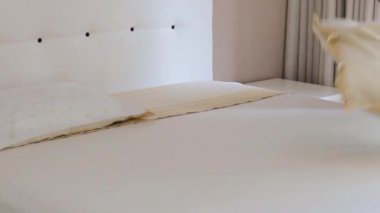 Bir kişi, yatak örtülerini ve yastıkları düzelterek, parlak, minimalist bir yatak odasında temiz ve düzenli bir uyku alanı yaratarak, yatağı yapma görevini dikkatle yerine getirir..