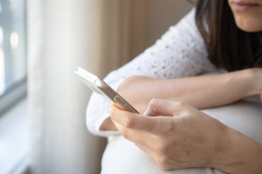 Bir kadın akıllı telefonu tutarken düşünceli bir şekilde oturur, dikkati ekrana odaklanır. Resim günlük hayatta tefekkür, bağlantı ve mobil teknolojiyi vurgular.