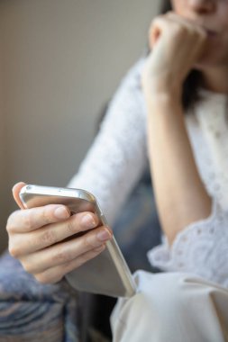 Bir kadın akıllı telefonu tutarken düşünceli bir şekilde oturur, dikkati ekrana odaklanır. Resim günlük hayatta tefekkür, bağlantı ve mobil teknolojiyi vurgular.