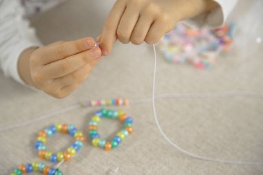 Bir çocuğun ellerinin renkli boncukları ipe geçirip el yapımı bir bilezik yapmaya odaklanması. Bu resim yaratıcılığı, iyi motor becerileri ve oyuncu öğrenmeyi yakalar..
