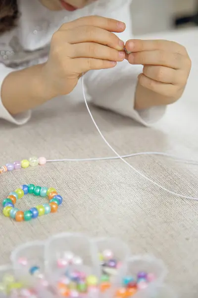 Bir çocuğun ellerinin renkli boncukları ipe geçirip el yapımı bir bilezik yapmaya odaklanması. Bu resim yaratıcılığı, iyi motor becerileri ve oyuncu öğrenmeyi yakalar..