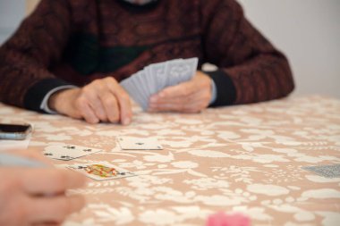 Bir grup insan bir masanın etrafında toplanır, aile veya arkadaşlarla gündelik bir oyun oynar, sosyal etkileşimi, arkadaşlığı ve bilişsel bağlılığı teşvik ederler..