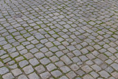 Düzensiz şekilli gri taşlar ve boşluklar arasında büyüyen yeşil yosun içeren kaldırıma yakın çekim, desenli ve doğal bir şehir geçidi deseni oluşturur. Portekiz kaldırımı