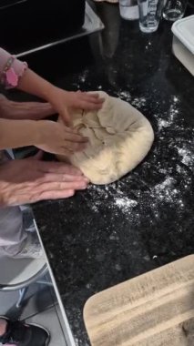 Bir çocuk ve bir yetişkin mutfak tezgahında hamur yoğurur. Ev yapımı ekmek yapımı ile aile bağlarını ve yaratıcılığı geliştiren ortak bir pişirme etkinliği sırasında bir ev mutfağında yakalandı..