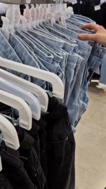 Bir müşteri bu ürünlerin seri üretimini göstermek için hızlı moda mağazasında kot pantolonlara göz atar. Bu video, perakende ortamda modern tüketici alışkanlıklarını ve moda seçimlerini yakalıyor..