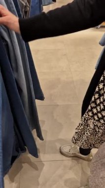 Bir müşteri bu ürünlerin seri üretimini göstermek için hızlı moda mağazasında kot pantolonlara göz atar. Bu video, perakende ortamda modern tüketici alışkanlıklarını ve moda seçimlerini yakalıyor..