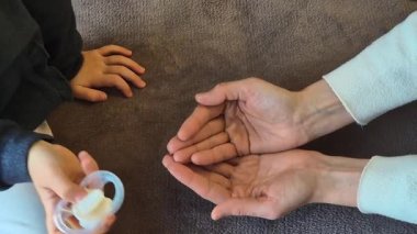 Bir çocuğun eli hasarlı bir emziği tutarken bir yetişkin asist aşırı kullanımdan gitmesine izin vermeye geçişi sembolize ediyor. Büyüme ve değişim dokunaklı bir an yatay bir videoda yakalandı..