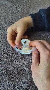 Bir çocuğun eli hasarlı bir emziği tutarken bir yetişkin asist aşırı kullanımdan gitmesine izin vermeye geçişi sembolize ediyor. Dikey bir videoda alınan dokunaklı bir büyüme ve değişim anı.