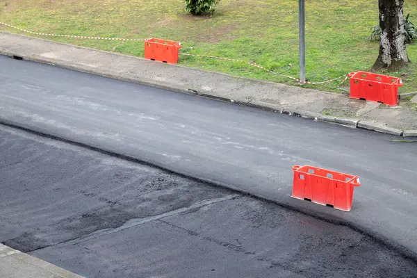 Yeni asfalt katmanlı yeni döşenmiş kamu yolu. Turuncu bariyerler güvenlik için yasak alanları işaretliyor.