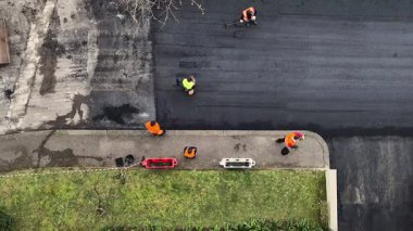 İşçiler kamu yoluna asfalt döşeyerek güvenlik, dayanıklılık ve trafik akışını iyileştirmek için ağır makineler kullanıyorlar. Bu kentsel yenileme altyapıyı geliştirir ve günlük kullanım için daha iyi koşullar sağlar.