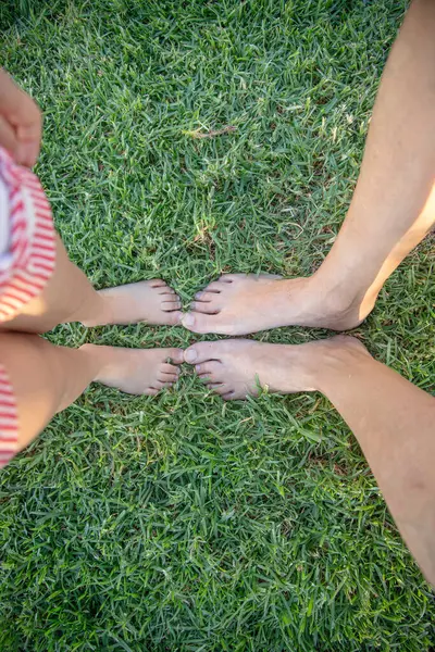 Yetişkin ve çocuk taze çimenlerin üzerinde yalınayak, ayak parmakları hassas bir anda birbirine dokunuyor. Bağlantının, sevginin ve basitliğin sembolü. Sıcak bir öğleden sonra birlikte doğanın tadını çıkarıyoruz..