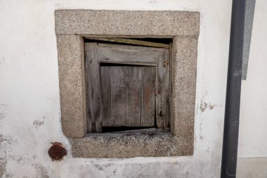 Eski ahşap bir pencere, granit taştan bir duvarda boyası soyuluyor. Tarihi bir köydeki mimari bozulmayı belgelemek için gündüz yapılan bir şehir keşfi sırasında çekilmiş..