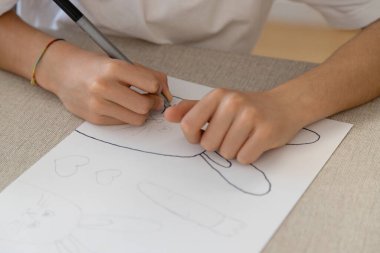 Bir çocuk, evde eğlenceli ve yaratıcı bir etkinlik sırasında tavşan, havuç ve kalplerin Paskalya temalı çizimlerini izler ve renklendirir. İnce motor becerilerini geliştiriyor..