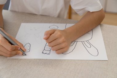 Bir çocuk, evde eğlenceli ve yaratıcı bir etkinlik sırasında tavşan, havuç ve kalplerin Paskalya temalı çizimlerini izler ve renklendirir. İnce motor becerilerini geliştiriyor..