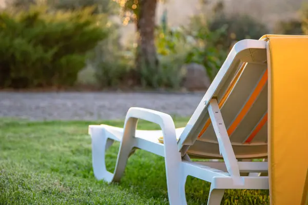 Sarı yastıklı plastik bir güneşlik, altın saatinde sessiz bir bahçede çimlerin üzerinde oturur, bir yaz tatili öğleden sonrası sükuneti, dinlenmeyi ve düşünmeyi davet eder..