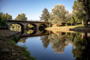 Sert, Portekiz 'de sıcak bir yaz öğleden sonrasında sakin bir nehir kenarı parkı. Kavisli köprü ve yansıması Castelo Branco bölgesindeki bu tarihi köyün ebedi cazibesini yansıtıyor..