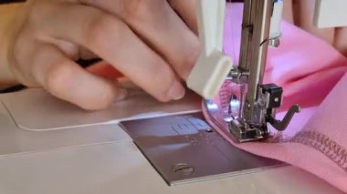 İç dikiş makinesine pembe kumaş diken, tekstil işçiliği yapan bir ortamda giysi yapımında hassas dikişlere odaklanan bir kişinin yakın çekimi..
