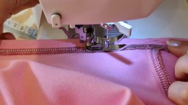 İç dikiş makinesine pembe kumaş diken, tekstil işçiliği yapan bir ortamda giysi yapımında hassas dikişlere odaklanan bir kişinin yakın çekimi..