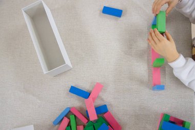 Genç bir çocuk gün içinde evde oynar, renkli ahşap bloklarla bir yapı inşa ederken dikkatle odaklanır, iyi motor beceriler, yaratıcılık ve erken bilişsel beceriler geliştirir..