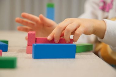 Genç bir çocuk gün içinde evde oynar, renkli ahşap bloklarla bir yapı inşa ederken dikkatle odaklanır, iyi motor beceriler, yaratıcılık ve erken bilişsel beceriler geliştirir..