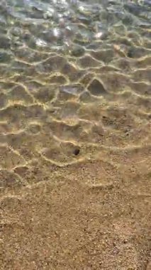 Kristal berrak deniz suyu, altın gibi kumlu bir sahilde yavaşça yıkanarak yüzeyin altındaki doğal dokuyu ortaya çıkarıyor, Porto Portekiz. Kapat.