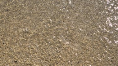 Deniz suyu, güneşli bir günde Portekiz 'in Matosinhos plajındaki kumlu zeminde yavaşça hareket ederek doğal dokuları, ışık yansımalarını ve kıyı hareketlerini yakalar..