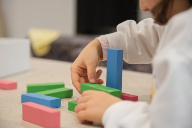 Genç bir çocuk gün içinde evde oynar, renkli ahşap bloklarla bir yapı inşa ederken dikkatle odaklanır, iyi motor beceriler, yaratıcılık ve erken bilişsel beceriler geliştirir..