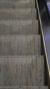 Modern bir binada yürüyen merdivenler iniyor. Görünürde kimse yok. Soyut perspektif, günlük geçişte kentsel hareketi, rutini ve mimari dokuyu vurgular. Kapat.