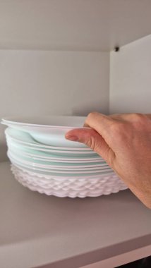 Ev işleri sırasında bir el mutfak rafında beyaz tabaklar düzenler. Ev idaresi ve düzen günlük kullanım ve yemek hazırlama için temiz ve işlevsel bir mutfak sağlar. Kapat.